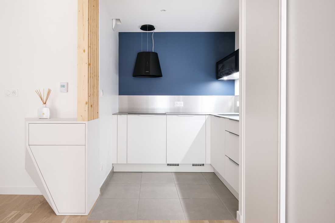 Cuisine blanche avec une forme en U et crédence bleue aménagée par un architecte d'intérieur dans un appartement neuf