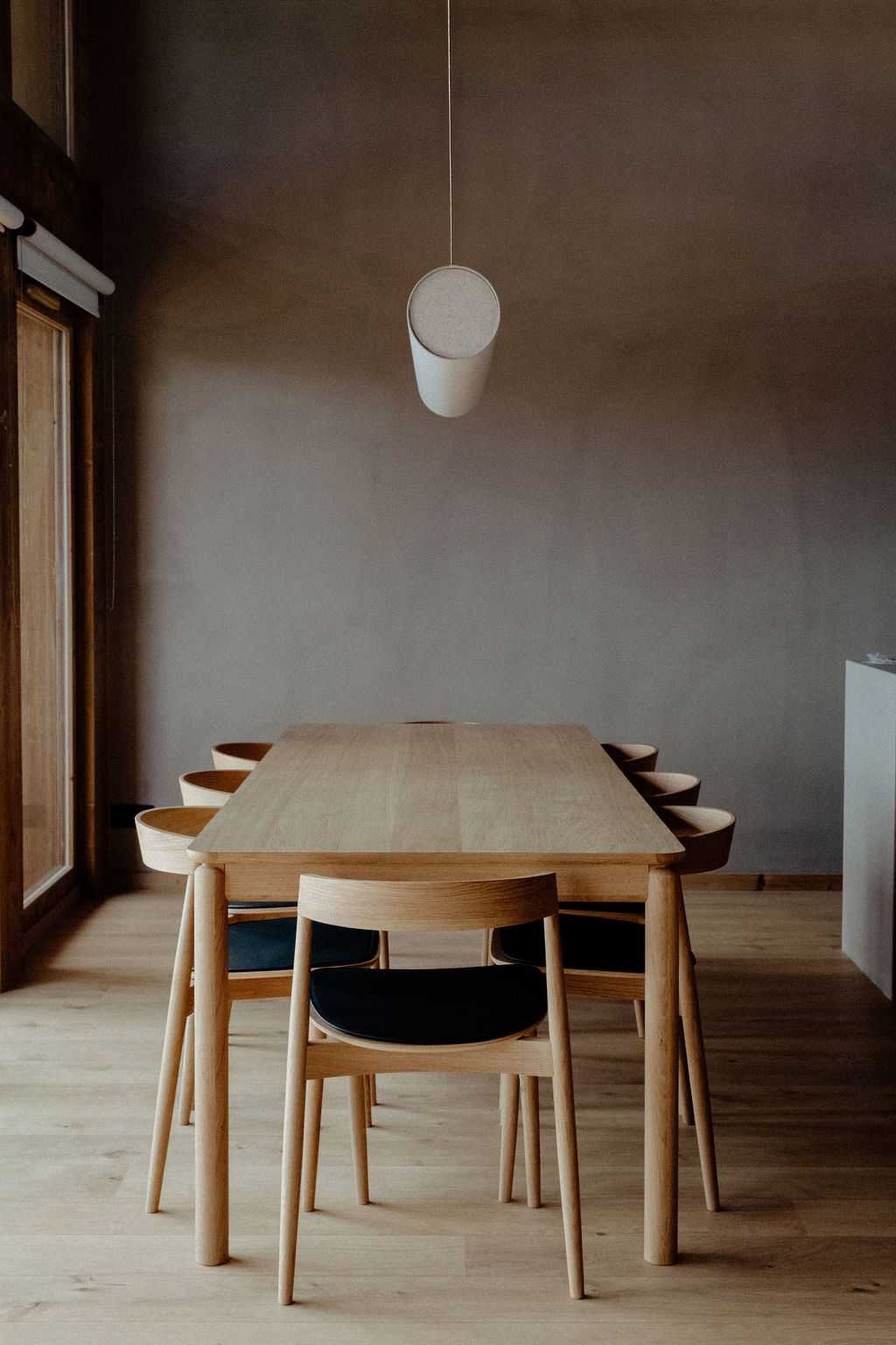 Salle à manger avec table en bois clair et suspension lumineuse cylindrique